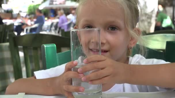 Gyerek ivóvíz az étteremben, Gyermek kezében egy pohár víz a teraszon, Kislány mosolygott, nevetett a kamerába — Stock videók