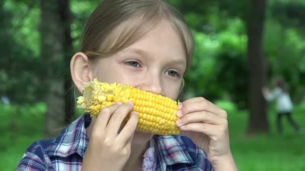 Criança comendo milho cozido ao ar livre no parque, garota faminta come comida saudável, criança loira jovem relaxante ao ar livre na natureza — Vídeo de Stock