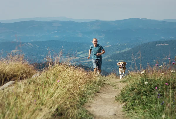 Hombre corre con su perro en la montaña — Foto de Stock