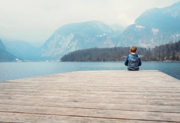 Kleine jongen zit op de houten pier — Stockfoto