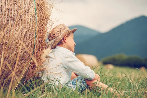 Niño se sienta cerca de pajar — Foto de Stock