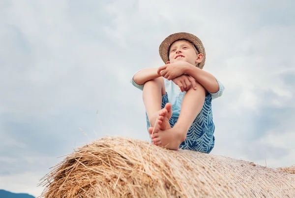 Chlapec sedí na hromadě sena — Stock fotografie