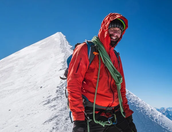 Rope team happy smiling man in climbing harness dressed red mountaineering clothes Last steps before Mont Blanc (Monte Bianco) summit 4808 m on the snowy slopes with a blue sky background.