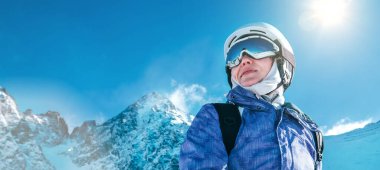 Skier female portrait in safe ski helmet and goggles with picturesque snowy Tatry mountains background. Active people winer vacation concept image.
