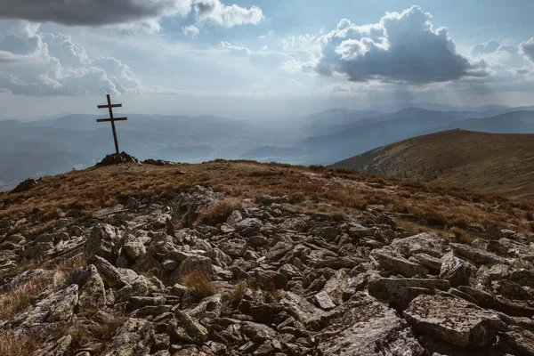 Patriarchal cross on the mountain summit with spectacular sun rays through the clouds. Low Tatras (Nizke Tatry) Crest Trail landscape view. Popular trekking path through the whole mountain range.