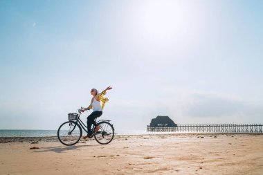 Hafif giyimli genç bir bayan, Zanzibar Adası 'ndaki Kiwengwa sahilinde, alçak dalgalı okyanus beyaz kumlu sahilde eski model bir bisiklete binerek sevinçle elini kaldırdı..