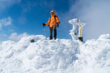  High mountaineer dressed bright orange softshell jacket on the snowy mountain summit.  Active people concept image on Velky Krivan, SLovakian Tatry. clipart