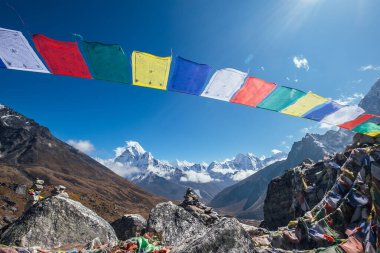 Kutsal Budist dua eden çok renkli bayraklar Vadi manzaralı güçlü rüzgar ve Ama Dablam 6812 metrelik zirvesiyle dalgalanmaktalar. Everest Merkez Kampı Dughla 4620 metre yakınındaki yürüyüş rotasında ilerliyor..