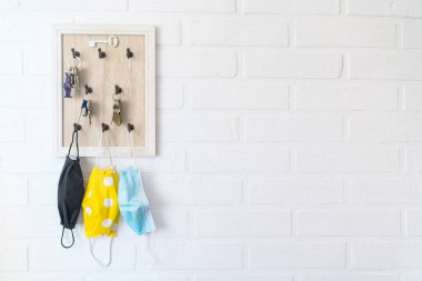 Anahtar düzenleyici kancadaki ağaç koruyucu maskeler ev koridorundaki beyaz arka plan tuğla duvara takılmış. COVID-19 pandemik konsept arkaplan görüntüsü sırasında sağlık hizmeti kavramı.