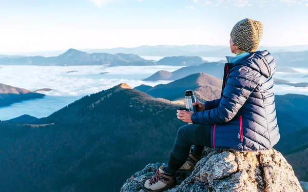 年轻的远足女性坐在山顶悬崖上 欣赏着布满云彩的山谷 成功攀登山顶的概念形象 — 图库照片