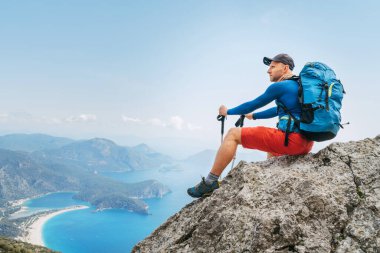 Genç sırt çantalı adam, Lycian Yolu 'ndaki yürüyüş sırasında uçurumda oturmuş Akdeniz Körfezi' nin tadını çıkarıyor. Meşhur Likya Yolu Türk rotası. Aktif spor insanları tatil konsepti imajı