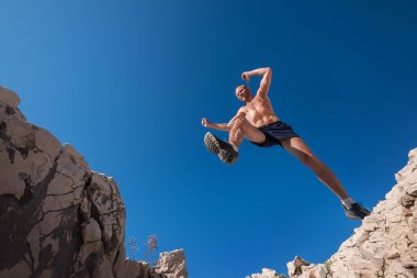 Yüksek sabah dayanıklılığı yarışında hızla koşan, gülümseyen ve uçurumdan atlayan aktif bir dağ koşucusu. Sportif insan aktiviteleri geniş açılı bir konsept görüntüsü.