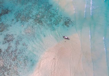 Aerial shot of the Mnemba Island white sand sandbanks washed with turquoise Indian ocean waves near the Zanzibar island, Tanzania. The couple came here on the motorboat, anchored it and having rest. clipart