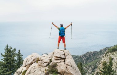 Genç gezgin sırt çantalı adam, Lycian Yolu yürüyüşü sırasında Akdeniz kıyısındaki kayalıkların üzerinde yürüyüş direklerini kaldırdı. Letoon yakınlarındaki ünlü Likya Yolu Türk rotası. Etkin tatil konsepti resmi