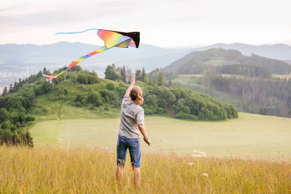 青山草甸上的少年推出了五彩缤纷的彩虹风筝长尾玩具 童年快乐时光或户外消磨时间的概念形象 — 图库照片