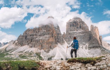 Dolomite Alpleri 'nde 2999 metre uzunluğundaki Tre Cime di Lavaredo formasyonunun keyfini çıkararak sırt çantasıyla ve yeşil dağ tepesinde yürüyüş direkleri ile yürüyen kadın yürüyüşçü. Aktif insanlar ve dağ konsepti