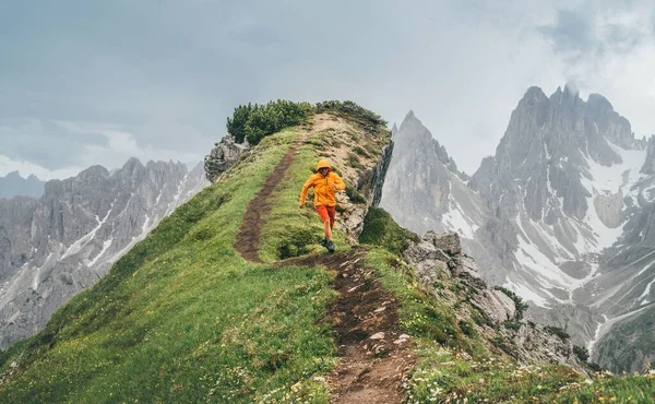 穿着亮丽的橙色软壳夹克跑步者 沿着绿色山路奔跑 背景为风景如画的白云石阿尔卑斯山 活跃分子与欧洲登山旅游概念形象 — 图库照片