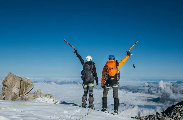 バックパック付きの登山服を着たカップルは 氷の斧で腕を上げ フランスのAiguille Midiの近くの頂上で景色を楽しんでいます 活動的な登山家や成功の概念イメージ — ストック写真