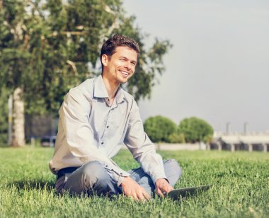 Adam otururken çimenlikte dizüstü bilgisayar ile