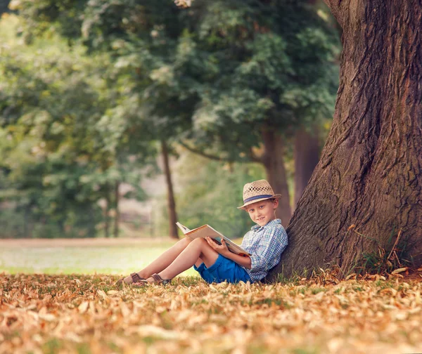 Junge mit Buch unter Baum sitzt — Stockfoto