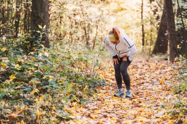 Sonbahar parkında sportif giyinmiş koşucu bir bayan sabah sarı sonbahar parkında koşarken şiddetli karın spazmı ağrısı içinde kıvranıyor. Etkin insanlar ve insan vücudu konsept görüntü sorunları
