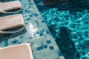 Güneşli mavi havuz suyu fayanslı kenarlı şezlongların yanında, tropikal tatiller, lüks tatil beldeleri, seyahat ve yaşam tarzı kullanımları için dinlendirici yaz tatilleri..