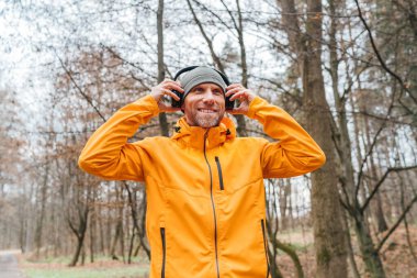 Gülümseyen orta yaşlı bir adam güz koşusu yapan şehir parkından zevk alıyor, müzik listelerini kulaklıklardan dinliyor enerjik hissediyor, açık hava aktiviteleri sırasında mutlu oluyor.