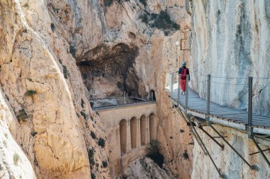 Genç bir kadın, Malaga İspanya 'da Caminito del Rey kanyonunda yürüyüş yaparken dik uçuruma bağlı dar tahta yolda yürürken sıra dışı maceralar ve güzel dağ manzarasının tadını çıkarıyor..
