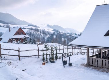Slovakya 'nın Terchova köyündeki geleneksel ahşap kulübelerde karla kaplı tepeler ve Mala Fatra Milli Parkı bölgesindeki bulutlu gökyüzü alanının altında dağ manzarası yer alıyor.