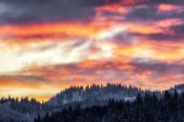 Akşam gökyüzünde renkli bulutlar ve arka planda kış dağları.