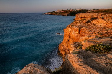 Evening view of rocky sea cliffs glowing red under sunset light with calm blue Mediterranean waters and dramatic coastline on Crete island, Greece.