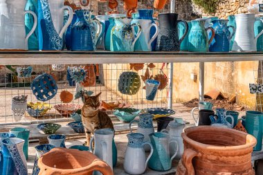 Margaritler, Girit, Yunanistan - 7 Eylül 2025: Yerel bir seramik dükkanında, geleneksel el sanatları ile tanınan köydeki renkli kil sürahileri ve vazolar arasında bir kediyle el yapımı çömlek sergilendi.
