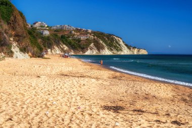 Byala, Bulgaristan - 25 Eylül 2025: Karadeniz kıyısındaki güneşli bir yaz gününde, sarp beyaz kayalıkların yakınındaki kumlu sahilde dinlenen ve yürüyen insanlar.