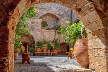 Yunanistan 'ın Girit kentindeki Toplou Manastırı' nın huzurlu iç avlusu, kil kaplar, taş duvarlar ve parlak güneş ışığı altında açan çiçeklerle.