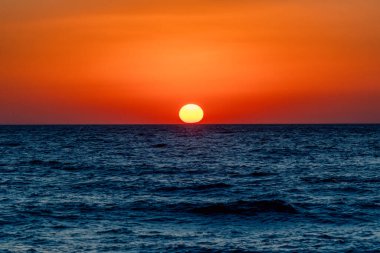 Yunanistan 'ın Girit kentindeki Kalamaki plajından çekilen, ufukta parlayan turuncu güneş ışığı ve berrak gökyüzü ile sakin denizin üzerinde güzel bir gün batımı..