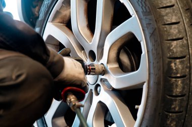 Tamirci tekerlek civatalarını lastik değiştirme sırasında pnömatik ingiliz anahtarıyla sıkıyor. Kıştan önce sezonluk araba bakımı ve güvenlik hazırlığı.