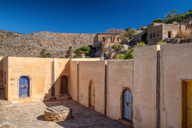 Yunanistan 'ın Girit kentindeki Spinalonga adasındaki geleneksel eski evlerin ve renkli ahşap kapıların manzarası, dağ manzarası ve arka planda açık mavi gökyüzü..