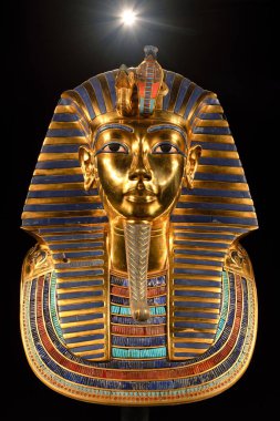 Tutankamon altın cenaze maskesinin ön görüntüsü karanlık bir arkaplanda sergileniyor, hiyeroglif detaylar vurgulanıyor, kraliyet sembolü ve geleneksel Mısır işçiliği.