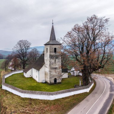Ludrova, Slovakya 'daki tarihi kilisenin, kırsal Liptov tarlaları ve sanayi bacalarıyla çekilmiş havadan çekilmiş fotoğrafı, miras mimarisi ve modern sanayi arasında bir zıtlık olduğunu gösteriyor..