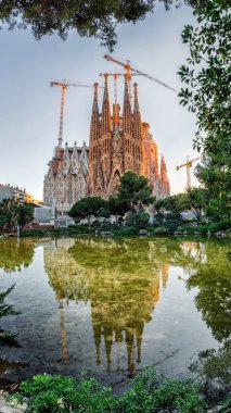 Barselona, İspanya - 17 Nisan 2020: La Sagrada Familia, devam eden çalışma sırasında bazilika etrafında inşaat vinçleri bulunan bir gölete yansıdı.