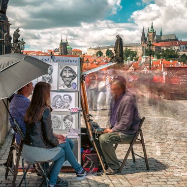 Prag, Çek Cumhuriyeti - 2 Temmuz 2017: Charles Köprüsü 'nde karikatür çizen sokak ressamı tarihi eser üzerinde ilerleyen bulanık turist kalabalığı.
