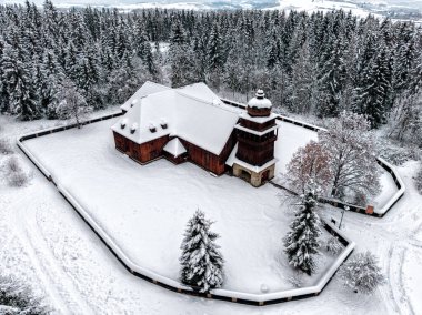 Slovakya 'nın Svaty Kriz kentindeki ahşap eklem kilisesinin tepeden aşağı insansız hava aracı görüntüsü net bir çapraz şekil oluşturuyor. Kar, kış ormanı manzarasında tahta protestan mimarisini kapladı..