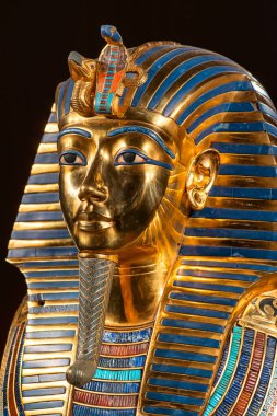 Eski Mısır Firavunu Tutanchamon olarak bilinen Kral Tut 'un altın cenaze maskesinin yakın portresi. Detaylı kraliyet yüzü ve koyu arkaplanda çizgili başlık.