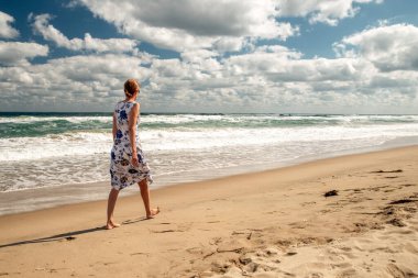 Bulgaristan 'ın Obzor kentinde Karadeniz kıyısında kumlu sahilde çıplak ayakla yürüyen bir kadın. Dramatik bulutlar ve dalgalar yaz seyahati ve özgürlük kavramı yaratır..