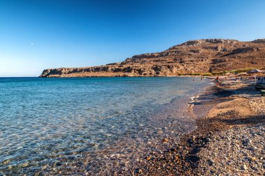 Yunanistan 'ın Girit kentinin güney kıyısındaki Kato Zakros' ta açık turkuaz deniz ve çakıl taşı plajı. Rocky tepeleri ve güneşli bir günde huzurlu kıyı manzarası.