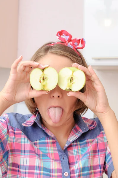 Chica joven feliz con dos manzanas cerca de sus ojos mostrando su dedo del pie Imágenes De Stock Sin Royalties Gratis