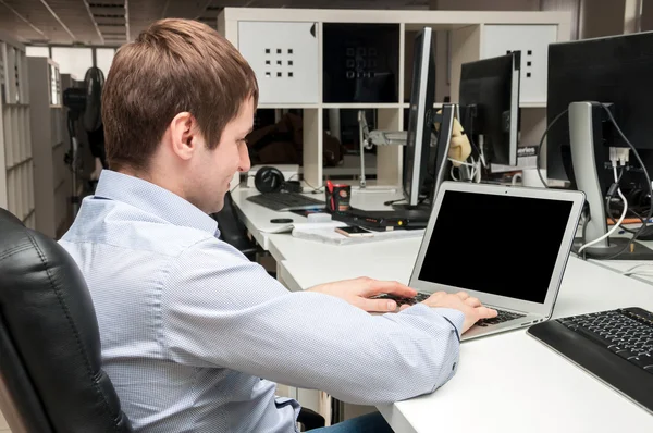 Jeune homme beau avec ordinateur dans le bureau. Réfléchir à la tâche dans la programmation — Photo