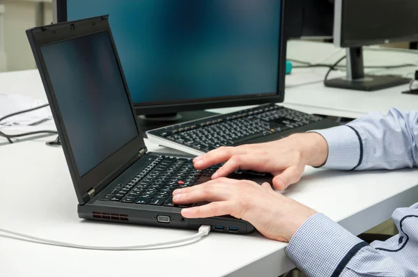 Jeune homme beau avec ordinateur dans le bureau. Réfléchir à la tâche dans la programmation — Photo