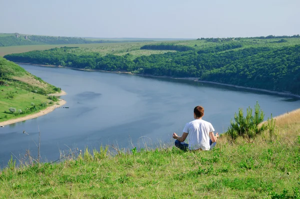 L'homme est assis au sommet d'une colline avec vue sur la rivière Dnister. Yoga medi Photos De Stock Libres De Droits