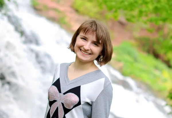 Young smiling girl posing near forest waterfall — Stock Photo, Image